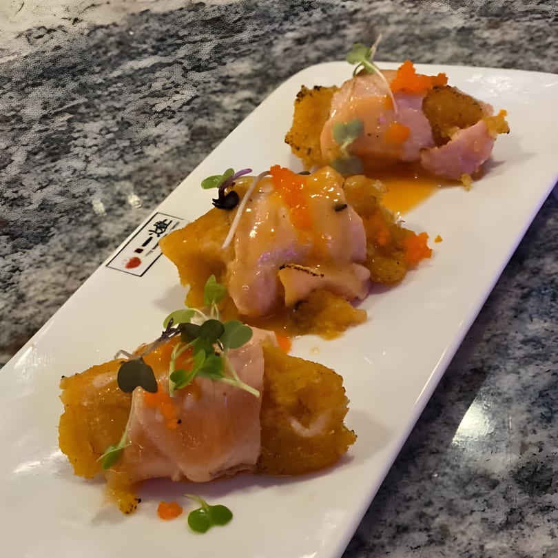 Three pieces of salmon sashimi on crispy rice, drizzled with sauce and garnished with microgreens.