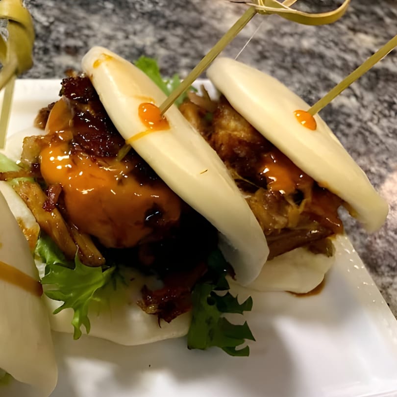 Itto Ramen Bar Tapas' pork belly bao buns with sauce and lettuce on a white plate.