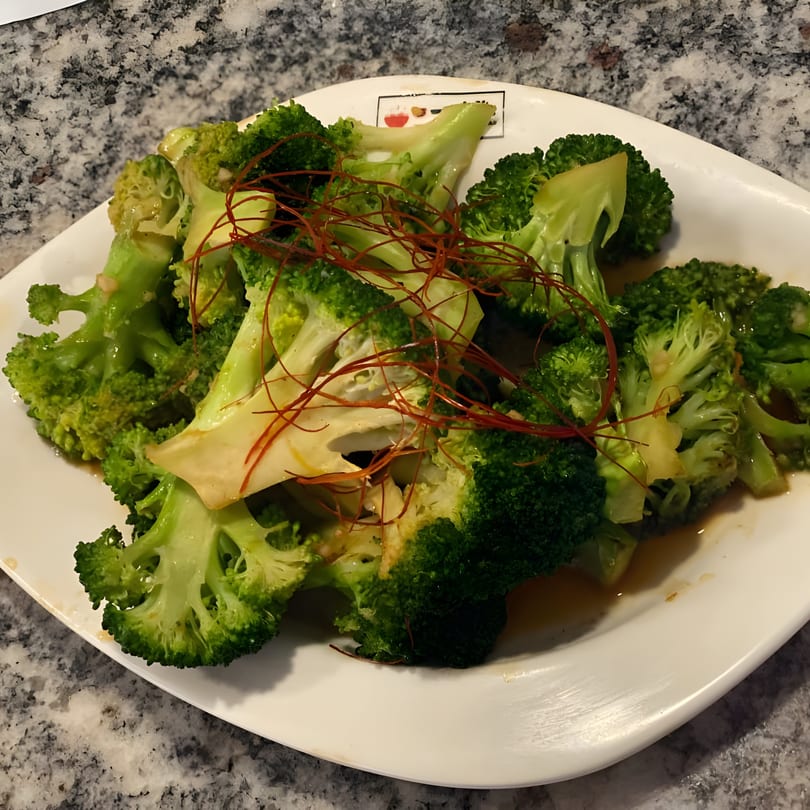 Steamed broccoli florets with red chili threads and a savory sauce on a white plate.
