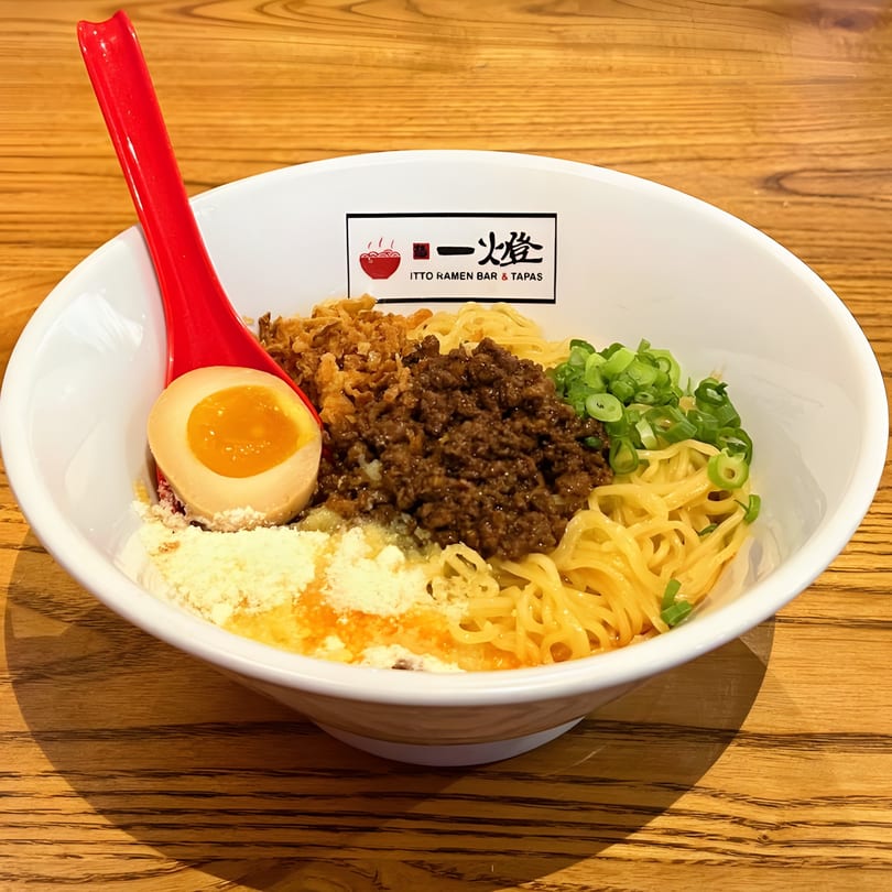 Itto Ramen Bar Tapas' ramen bowl with noodles, ground meat, scallions, egg, and a red spoon.