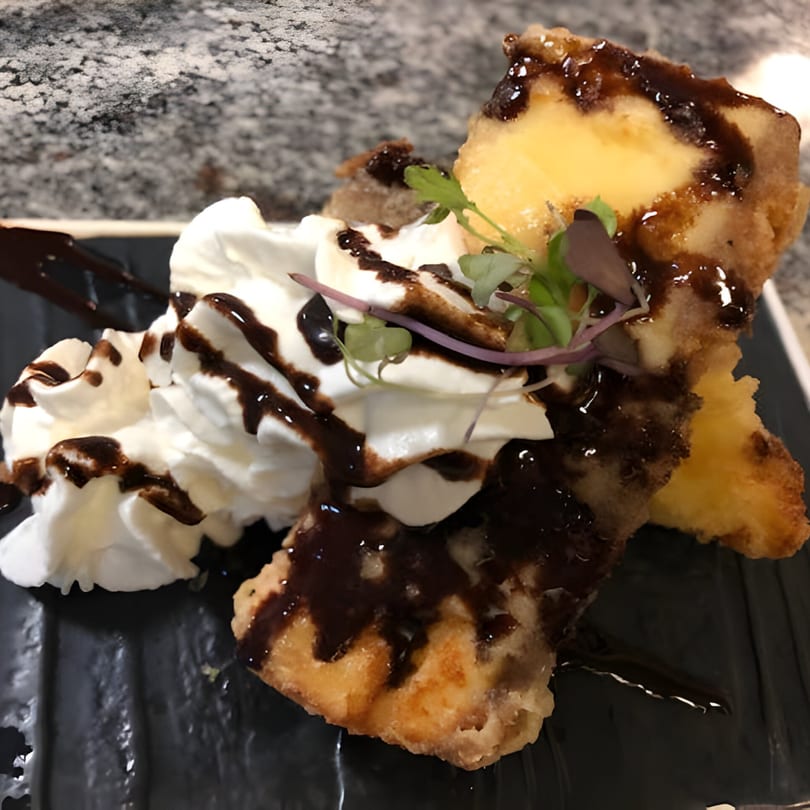 Fried ice cream dessert with whipped cream, chocolate drizzle, and microgreens on a black plate.
